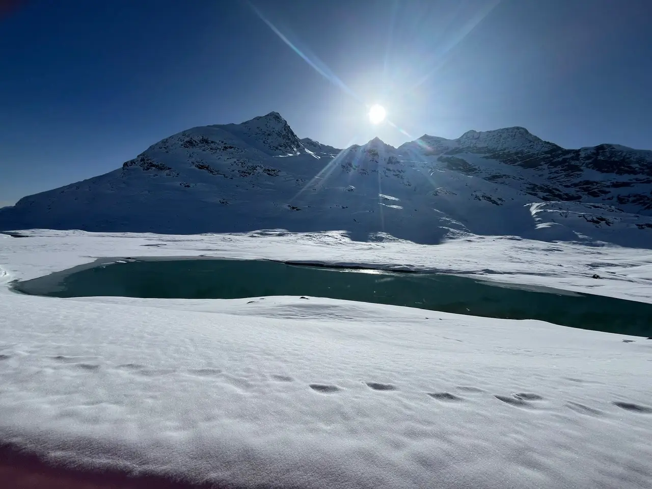 Lago Bianco at the Bernina Pass — a vivid turquoise glacial lake partially frozen, surrounded by snow and mountains