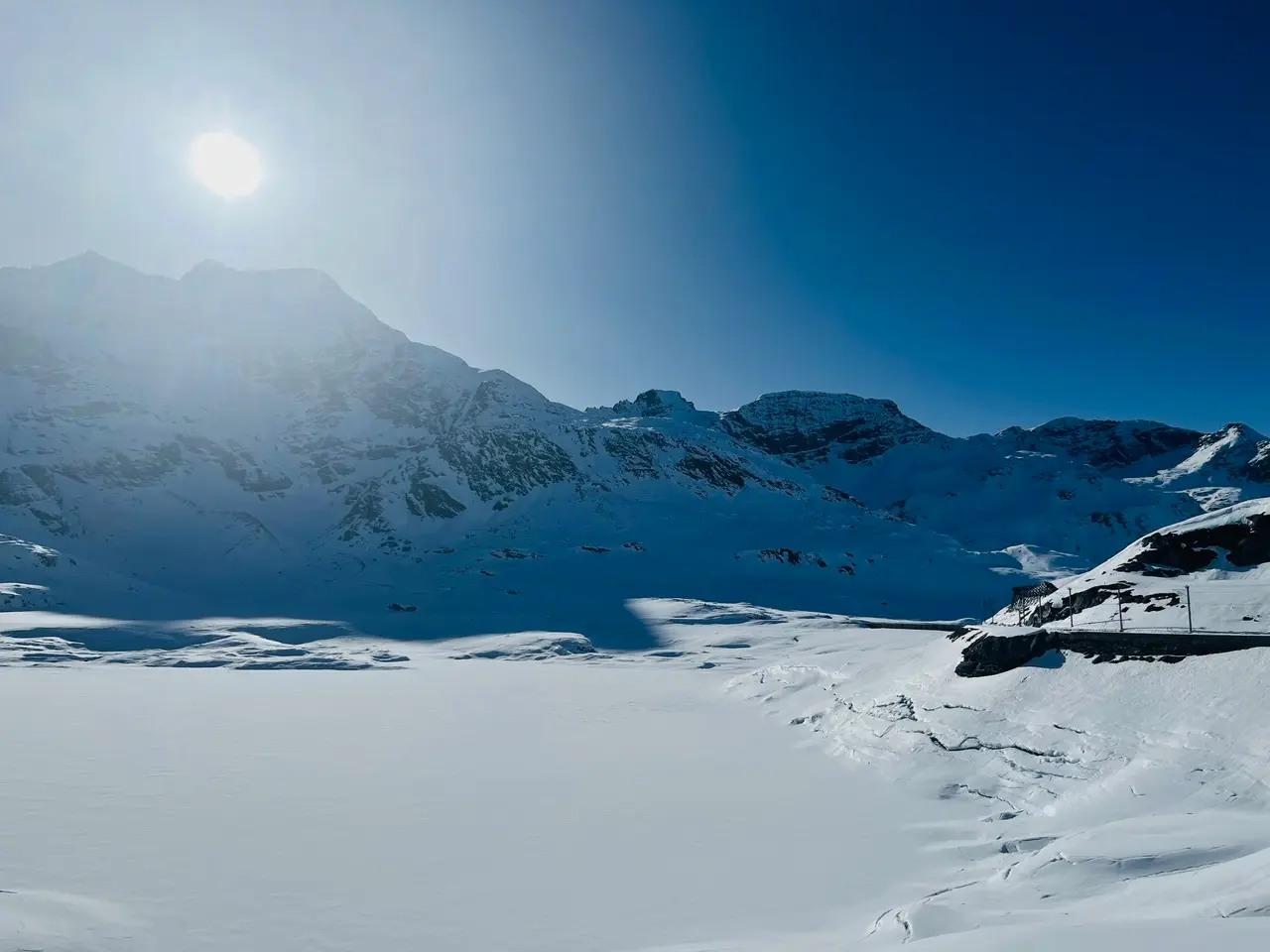 Lago Bianco fully frozen and snow-covered at the Bernina Pass, with the Alps rising steeply behind