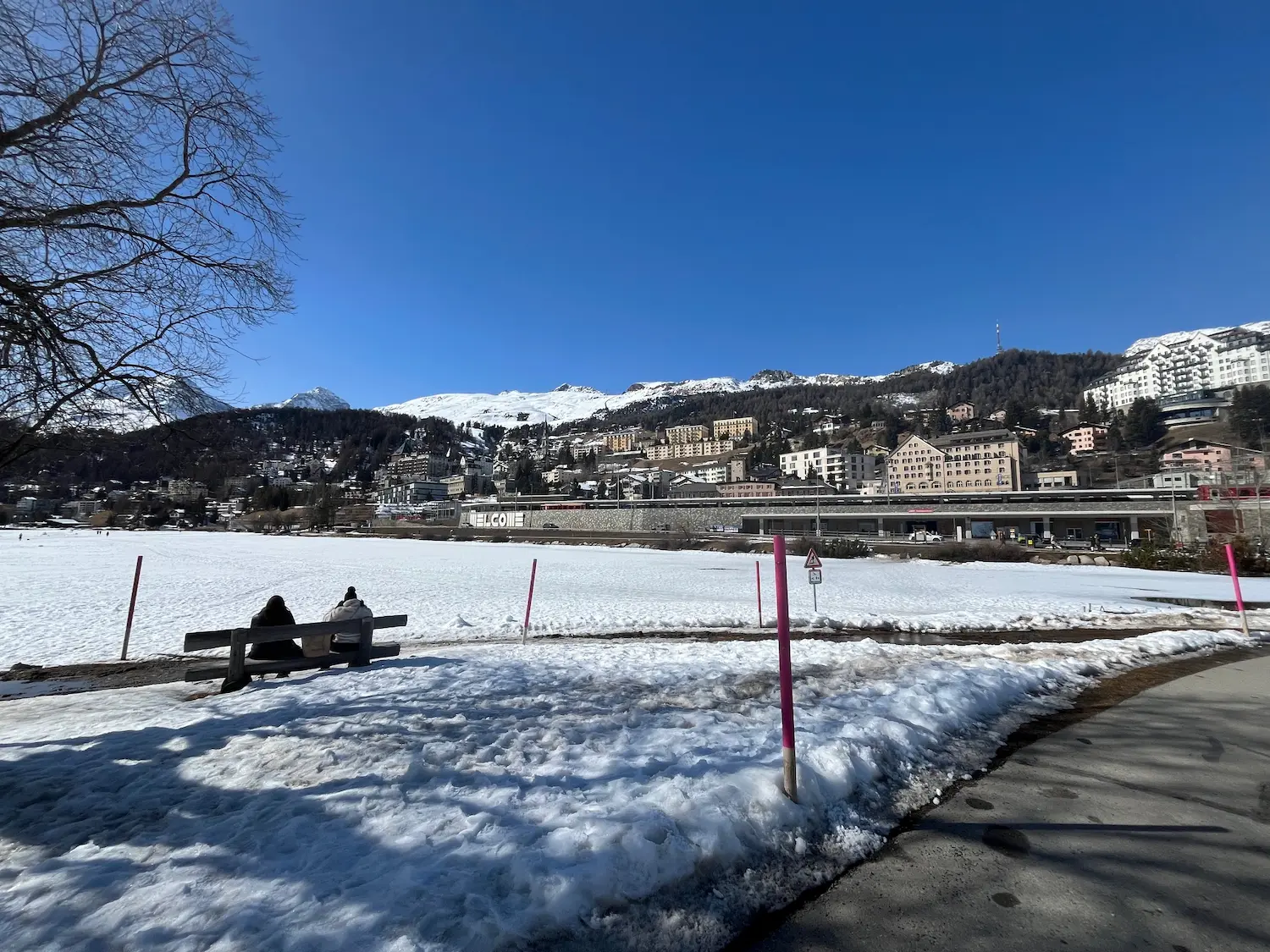 St Moritz town and hotels above the frozen lake, viewed from the lakeside path in winter