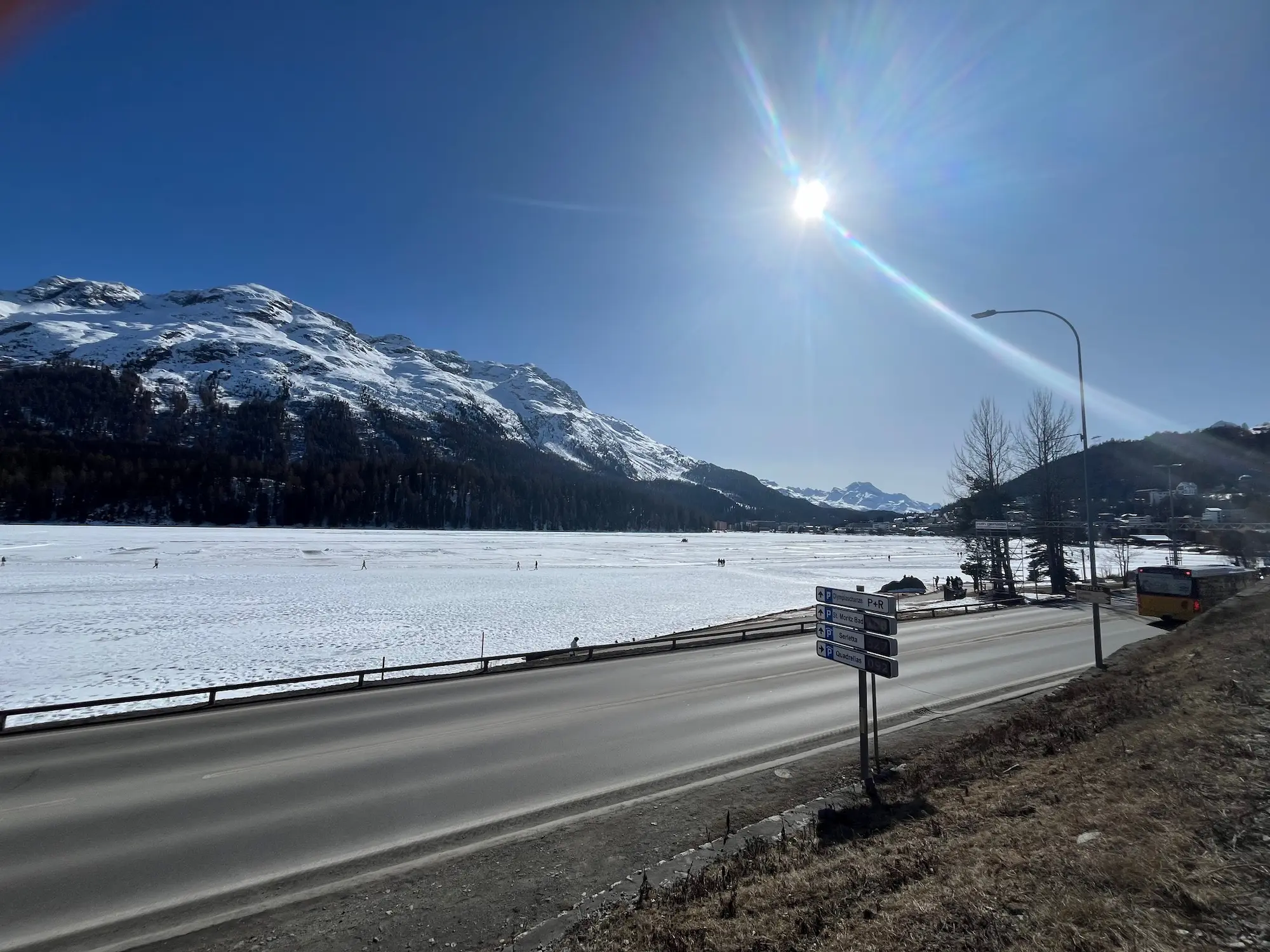 Lake St Moritz from the road in winter — completely frozen, with the Alps reflected in the deep blue sky above