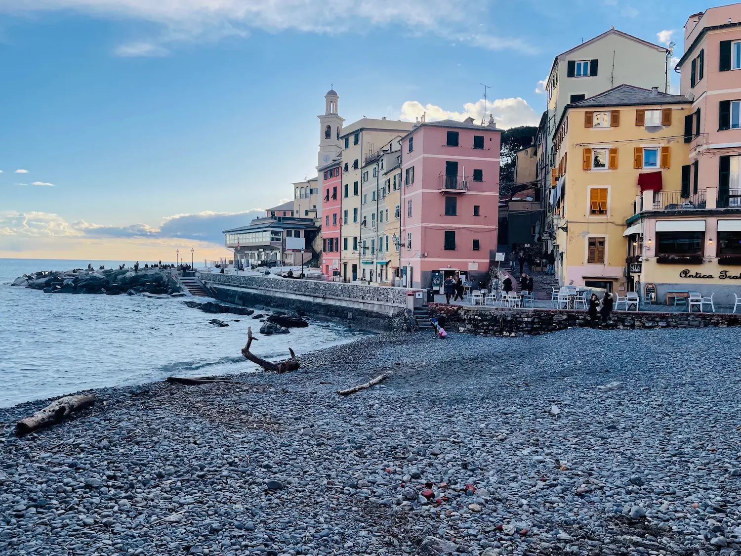 Boccadasse beach and colourful fishermen's houses from the pebble shore, with a fishing boat in the foreground and the Ligurian Sea beyond
