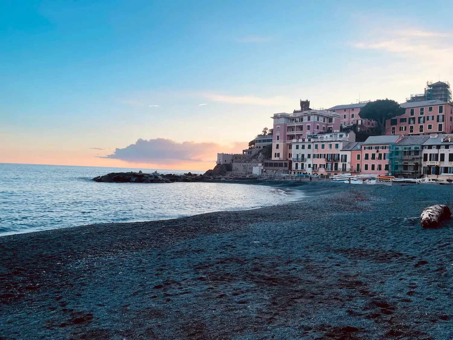Boccadasse waterfront at dusk — colourful houses, a church tower and the seafront promenade reflected in the calm evening light