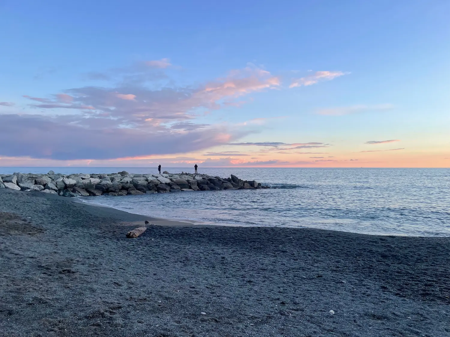 Boccadasse cove at sunset — pink and blue sky over the Ligurian Sea, with the village buildings rising on the rocky headland