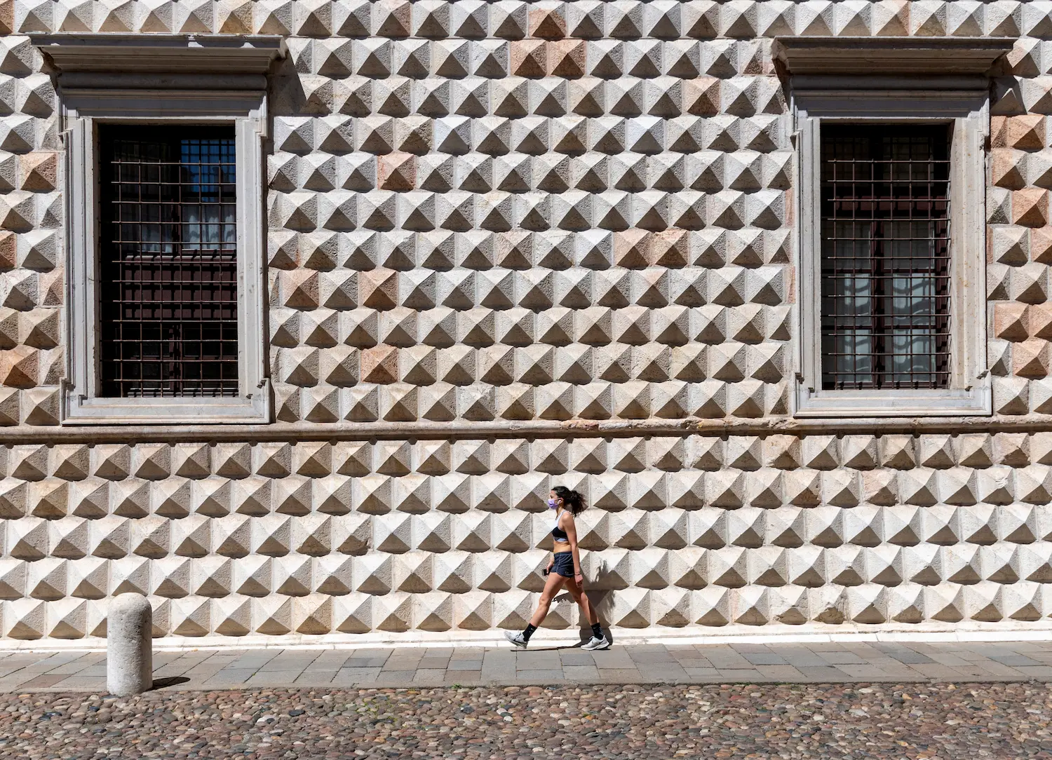 A figure walks past the diamond-pointed marble facade of the Palazzo dei Diamanti, Ferrara — each block carved into a pyramid shape that catches the light at a different angle