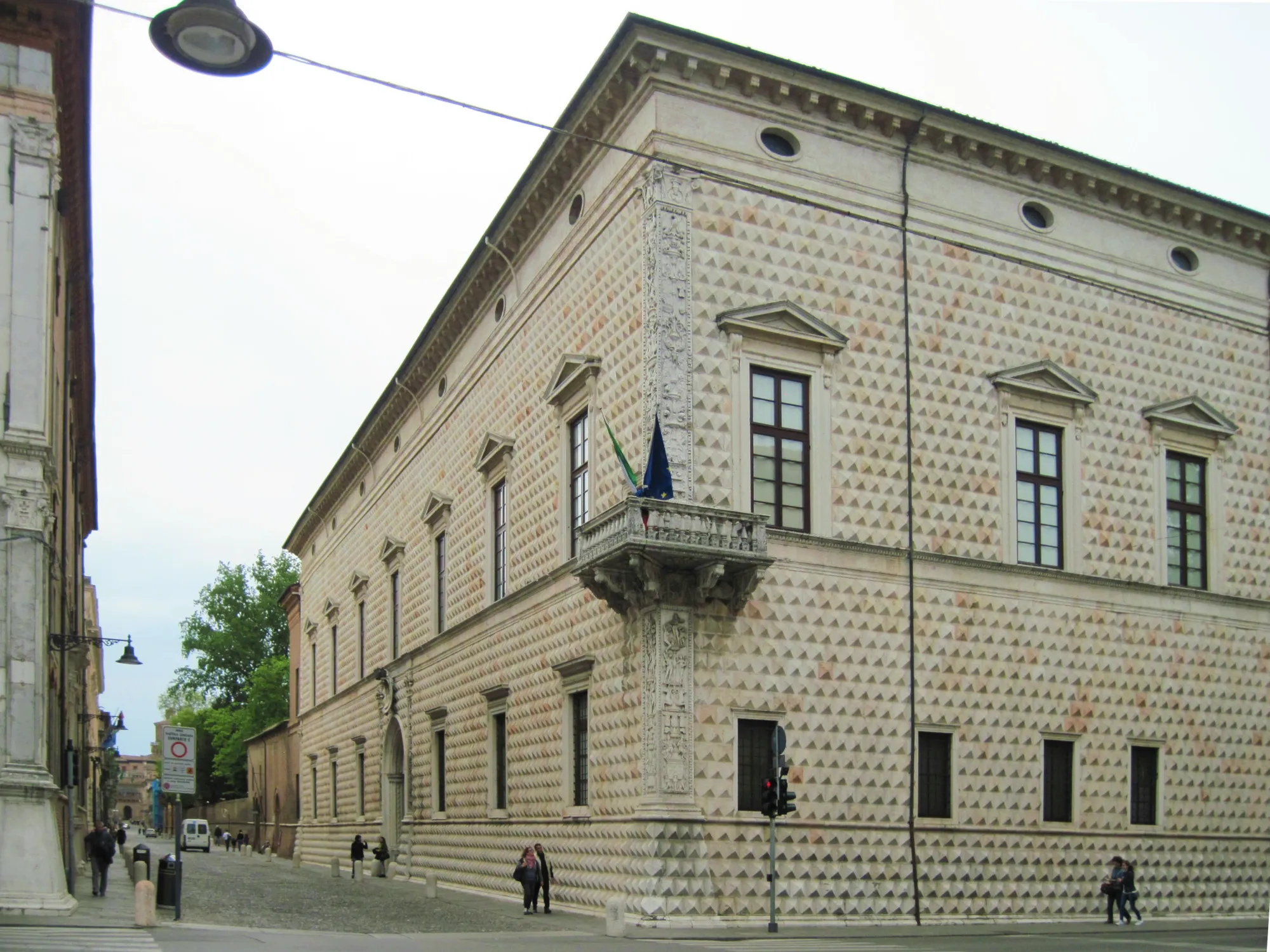 The full facade of the Palazzo dei Diamanti on Corso Ercole I d'Este, Ferrara — the entire building covered in 8,500 marble diamond-pointed blocks, with the ornate corner column visible