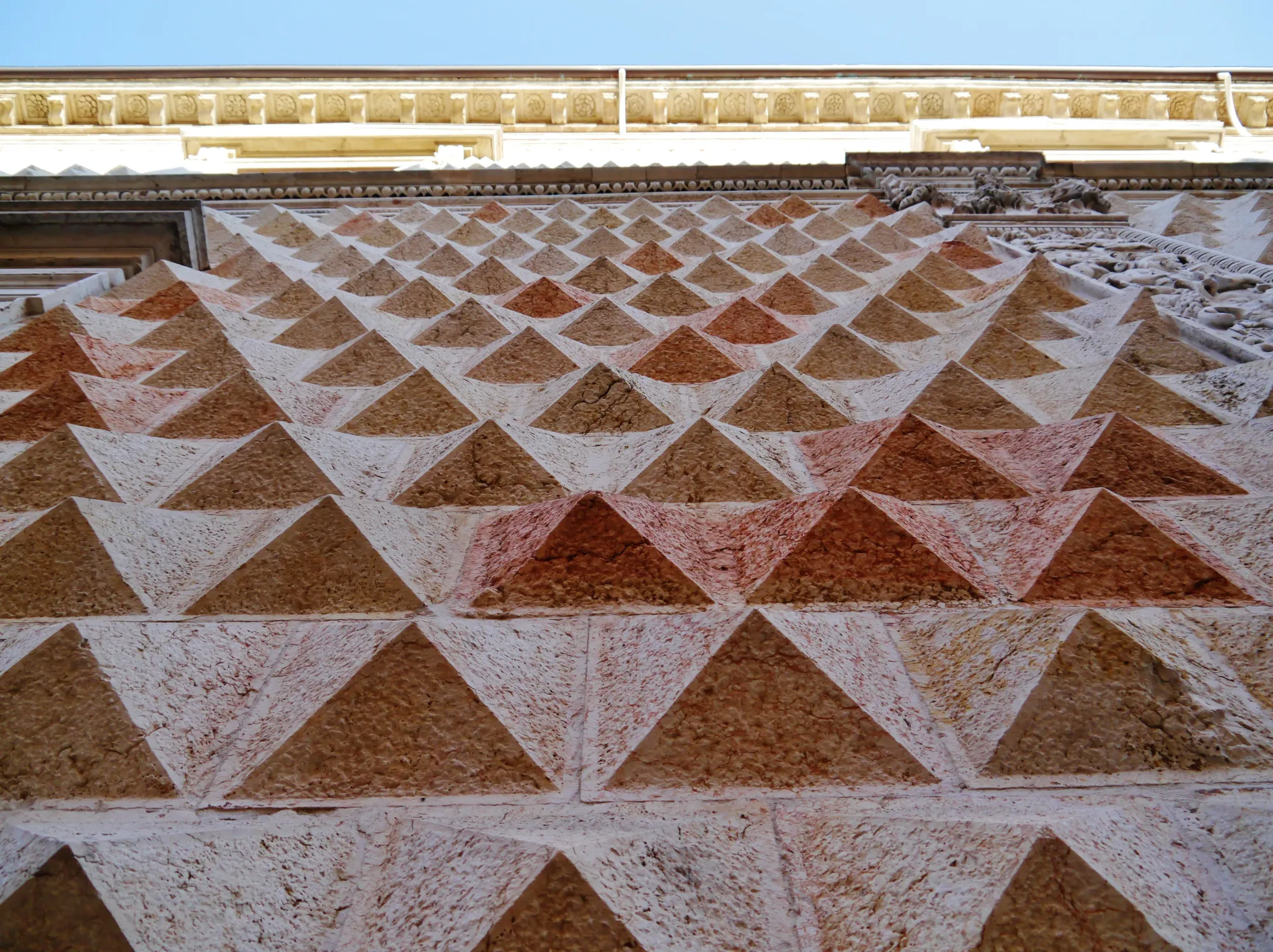 Close-up detail of the diamond-pointed marble blocks of the Palazzo dei Diamanti, Ferrara — the terracotta and cream tones of the stone visible in the afternoon light
