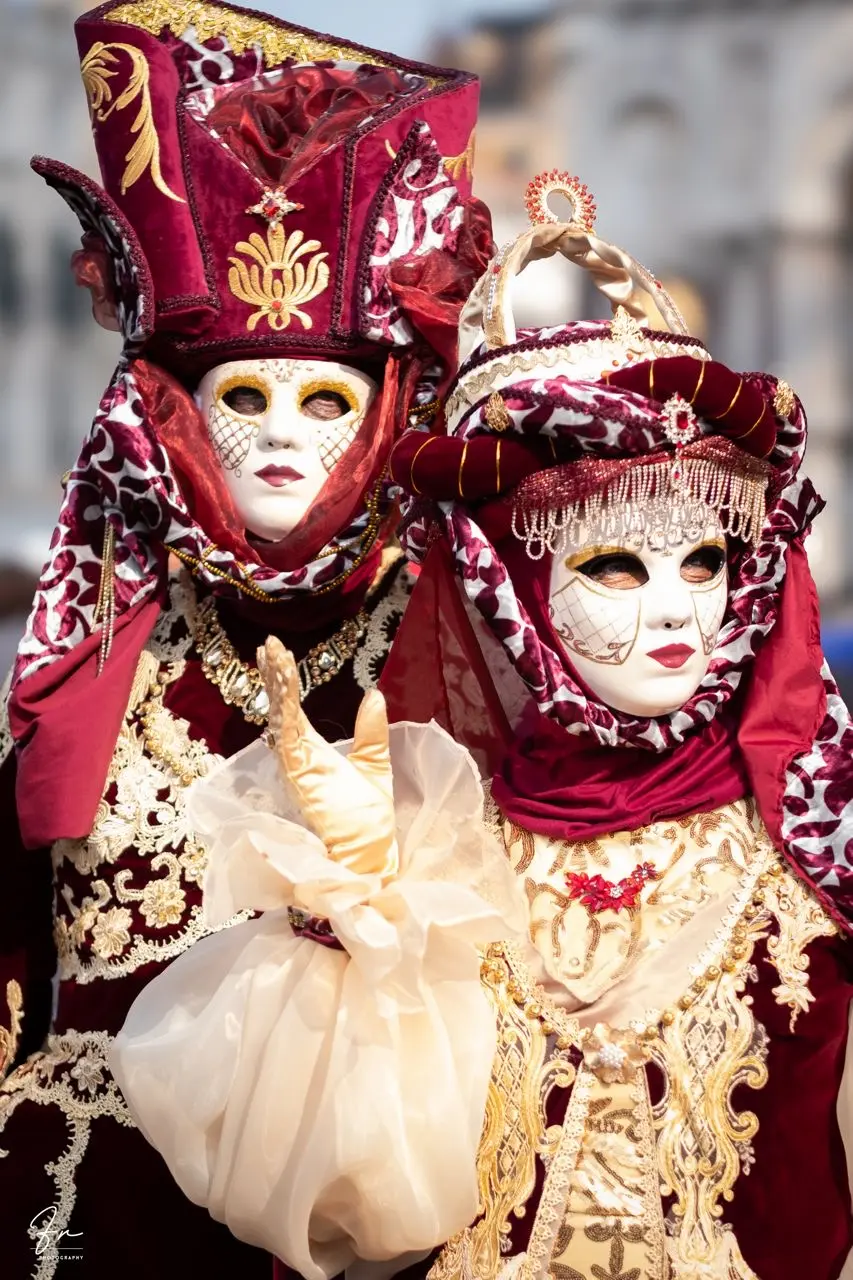 Two masked revellers in burgundy and gold velvet Carnival costumes with ornate feathered headdresses, Venice