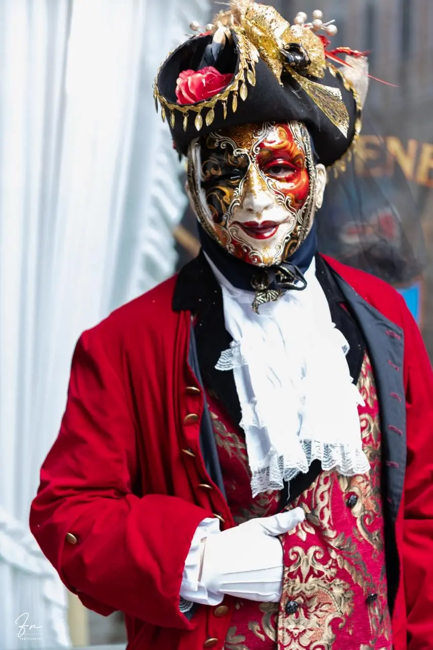 Carnival reveller in red velvet coat and gold tricorn hat with a painted red and gold mask, Venice