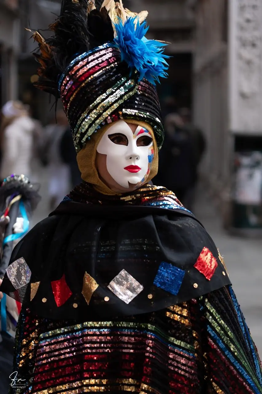Carnival reveller in a sequinned rainbow cape and feathered turban, Venice