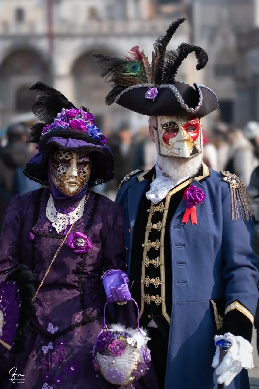 Couple in purple Victorian-style gown and navy military-style coat, masked for Venice Carnival